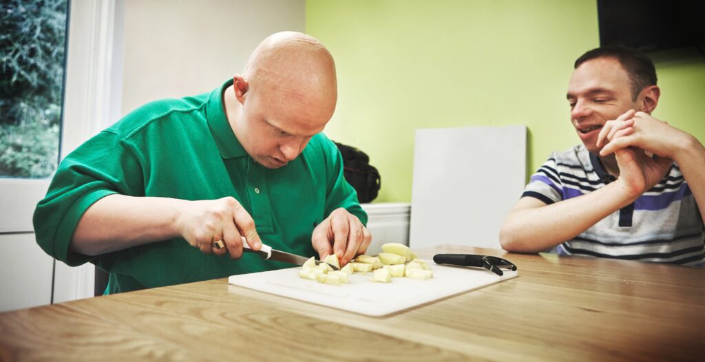 adult man with green shirt cutting vegetables in a cooking class for IDD people 