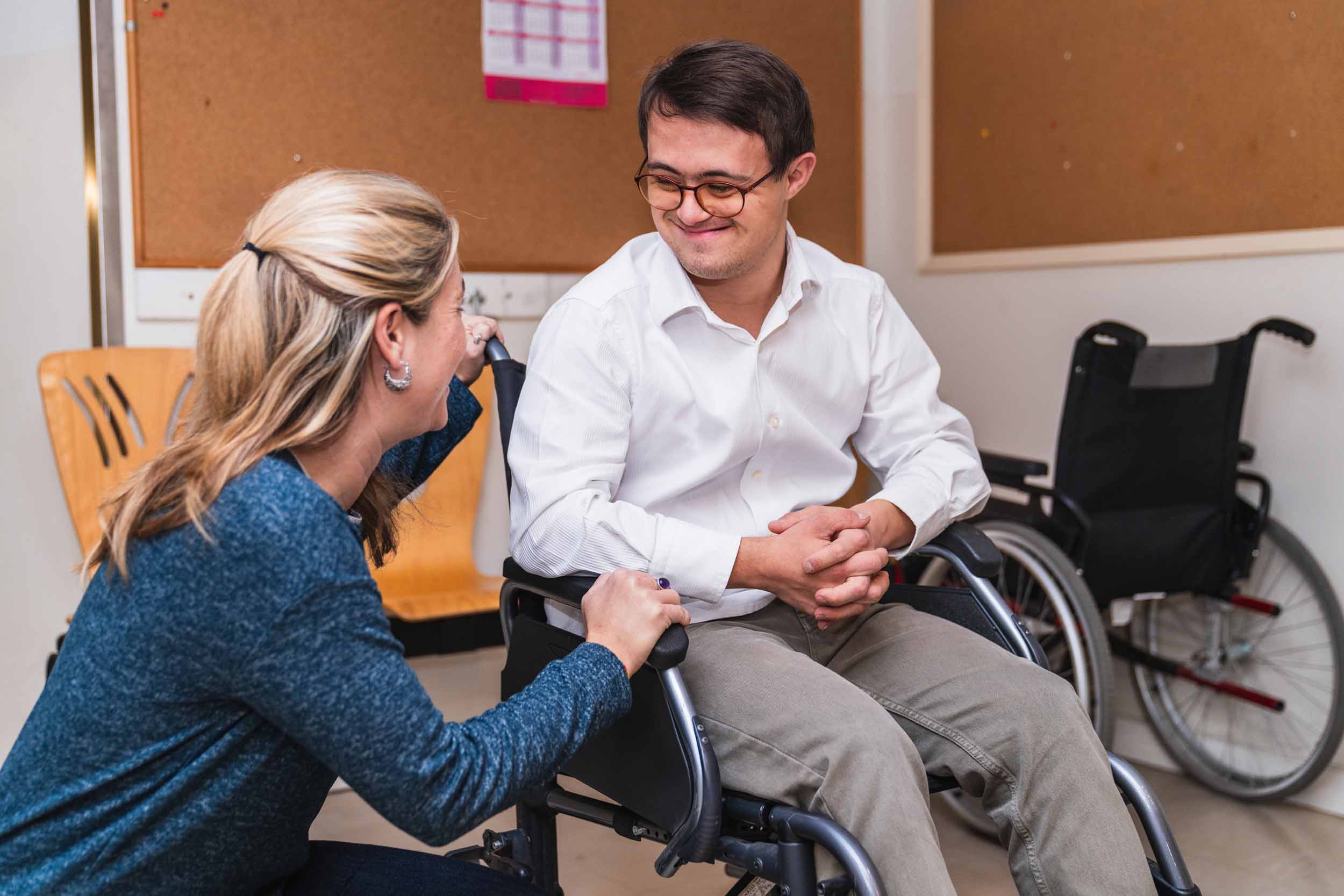 A caring moment of connection between a woman and a man with Down syndrome in a wheelchair.