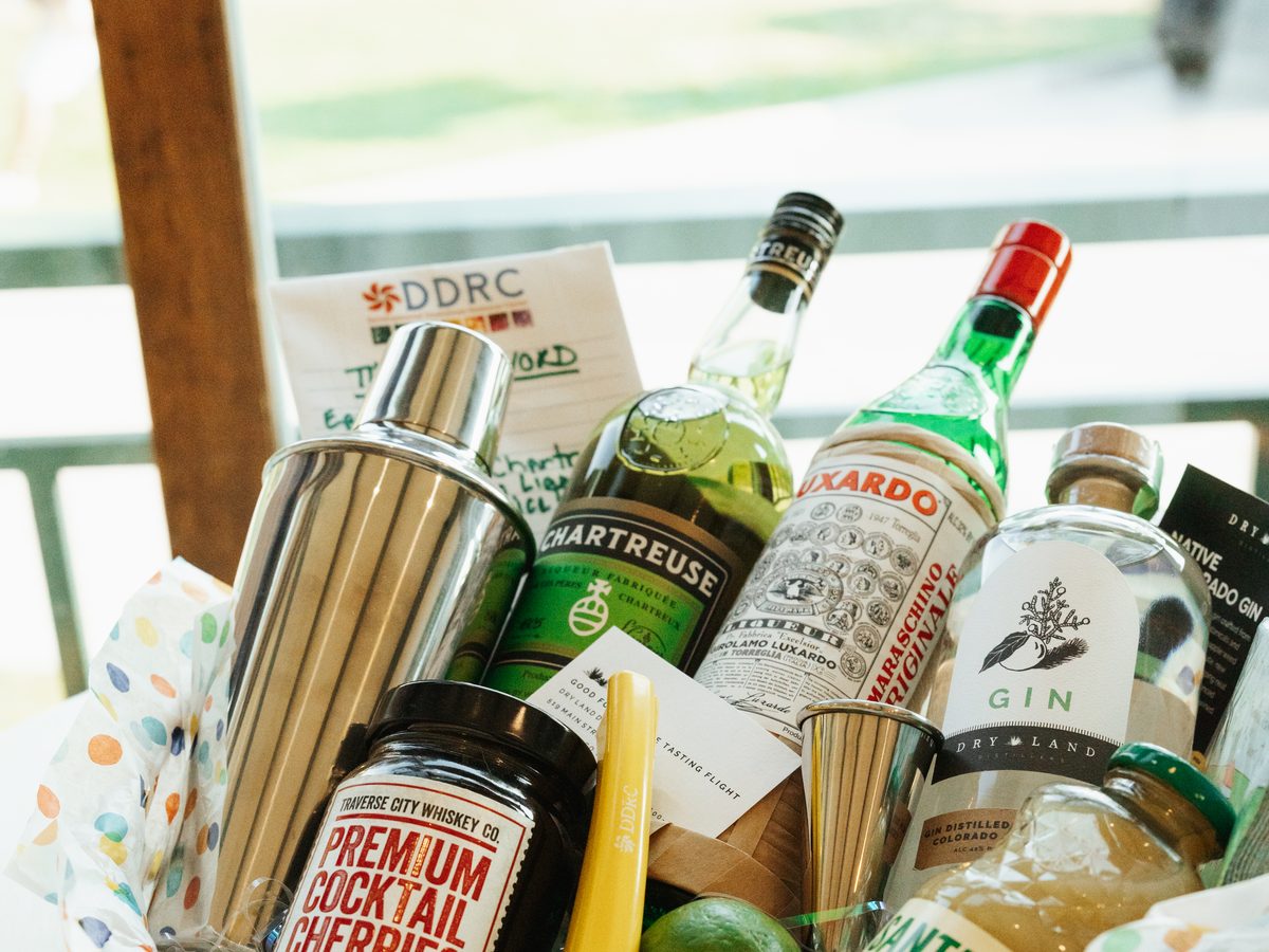 Auction gift basket filled with cocktail mixers, spirits, and bar tools, tagged with the DDRC logo