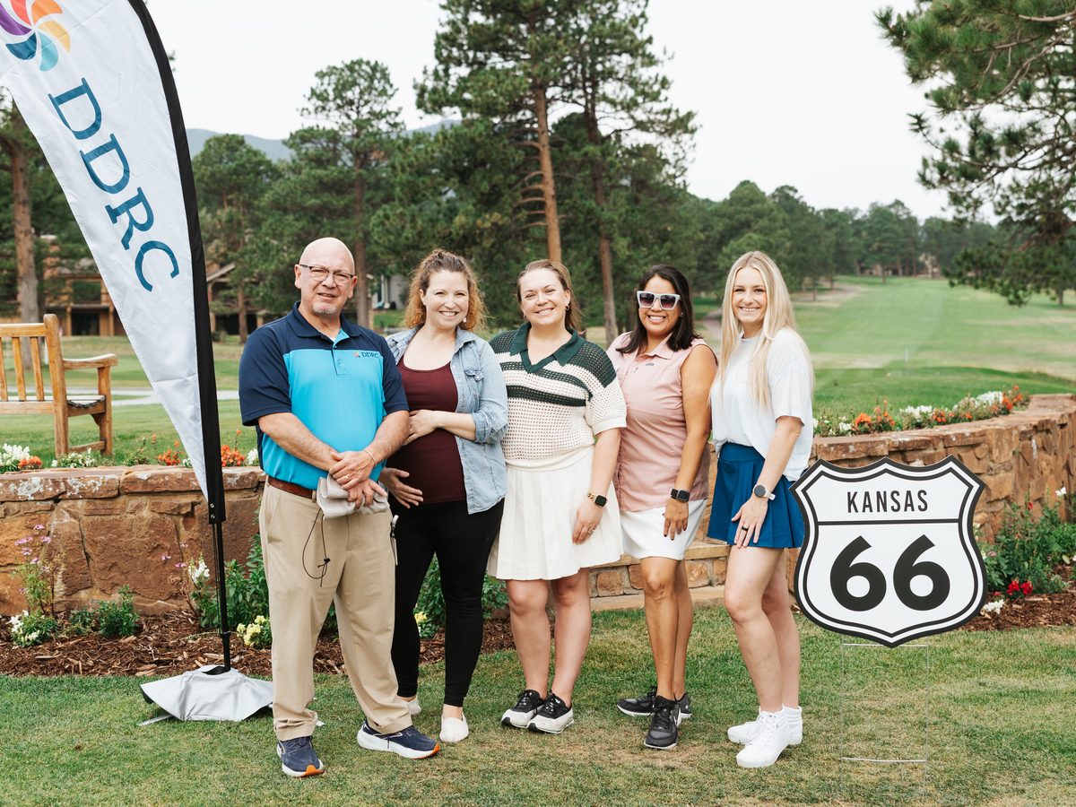 Five people smile together on the course beside a DDRC flag and a Kansas Route 66 sign