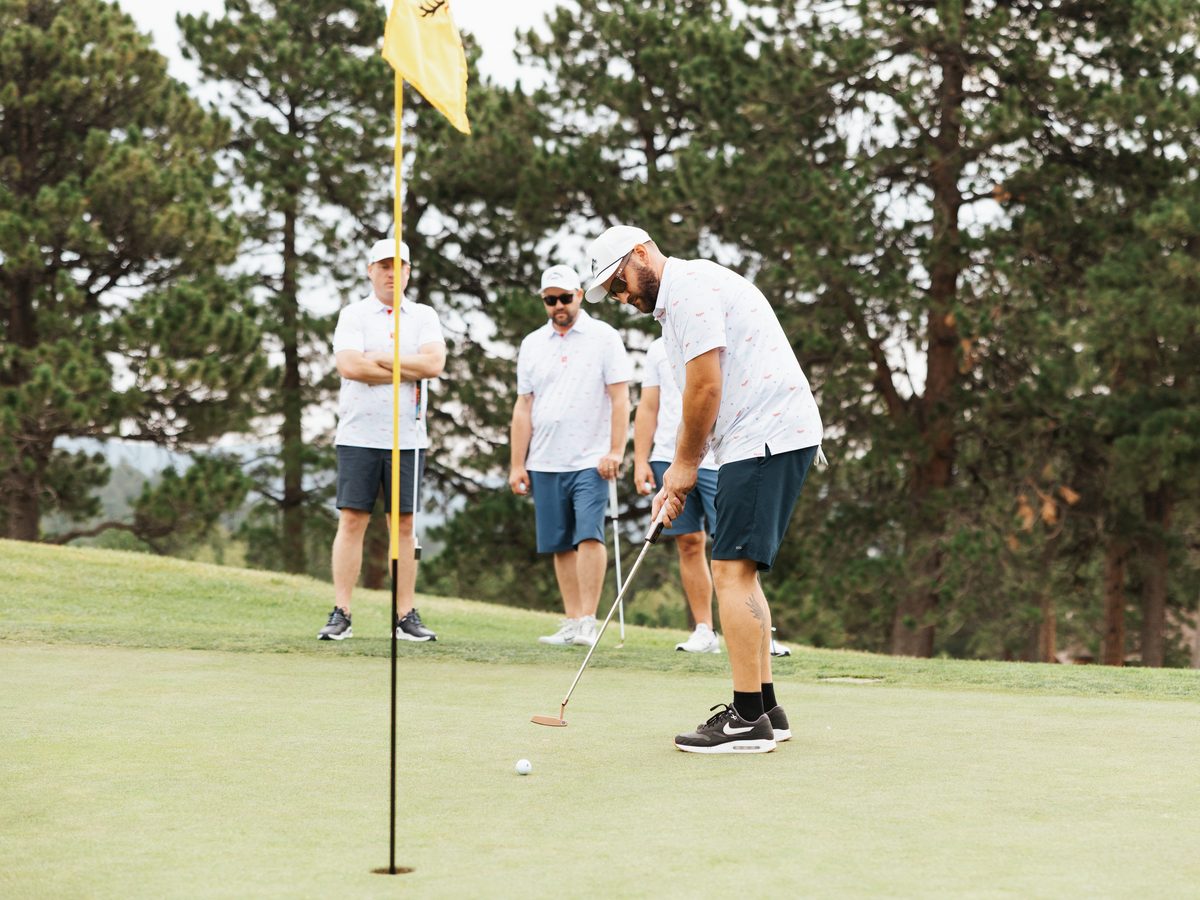 A golfer lines up a putt on the green while three teammates watch beside the flagstick