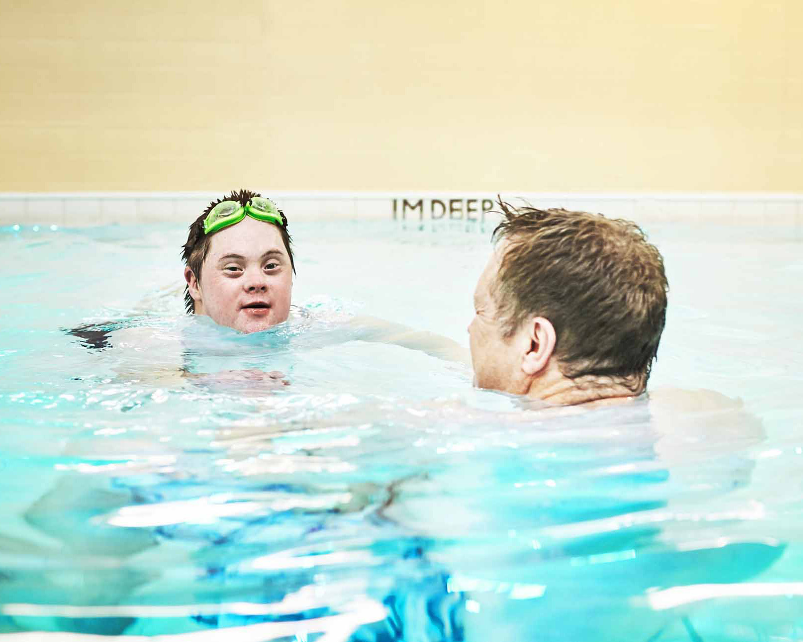 Man with down syndrome swimming in a pool during a sports class with a swim instructor.